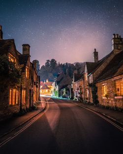 Road amidst buildings against star field at night