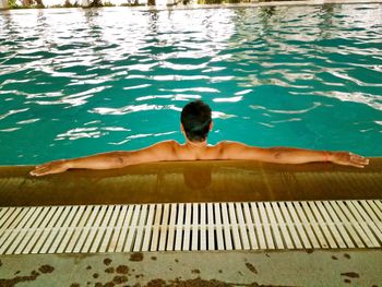 Rear view of shirtless man with arms outstretched in pool