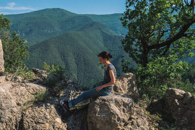 Side view of man sitting on rock against mountains