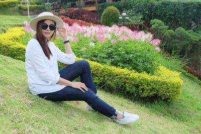 Portrait of beautiful woman sitting on grassy field against plants at park