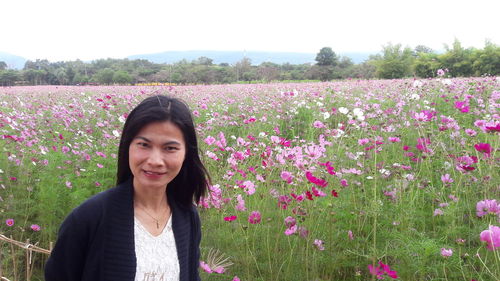 Portrait of smiling mature woman standing against pink flowers