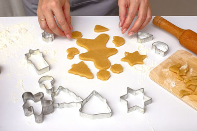 Female hands cut out christmas cookies from dough, using metal molds, on a white table.