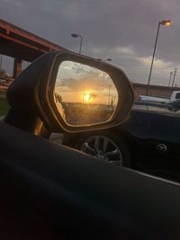 Close-up of side-view mirror against sunset sky