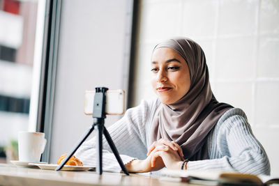Portrait of young woman holding coffee while sitting on table