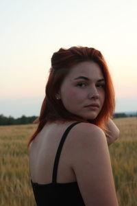 Portrait of beautiful woman standing on field against sky during sunset