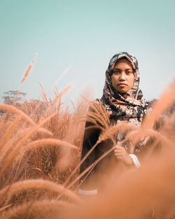 Portrait of woman standing amidst grass on field against clear sky