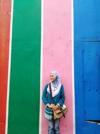 Full length of smiling young woman standing against colorful wall