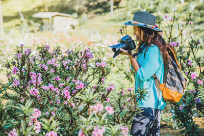 Side view of young woman photographing flowers from camera on land
