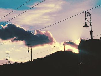 Low angle view of electricity pylon against cloudy sky