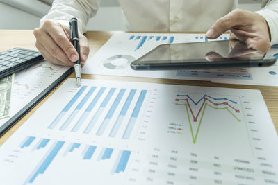 Midsection of man with digital tablet analyzing chart on table