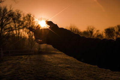 Silhouette hand holding sun during sunset