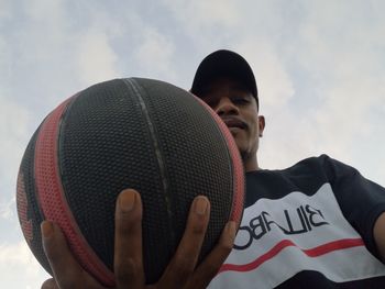 Portrait of young man holding camera against sky