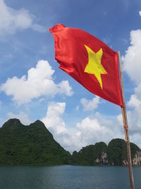 Vietnamese flag by sea and mountains against sky