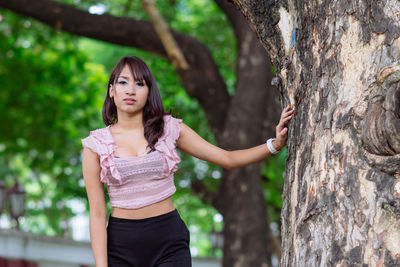 Portrait of young woman standing by tree trunk