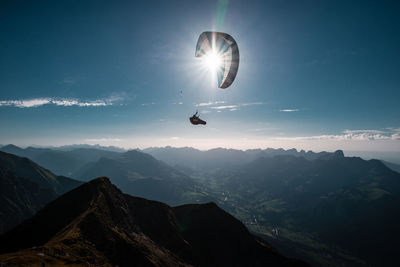 Man paragliding over mountains against sky during sunny day