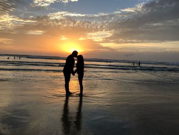 Silhouette people on beach against sky during sunset