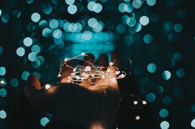 Cropped hand of woman holding illuminated christmas lights