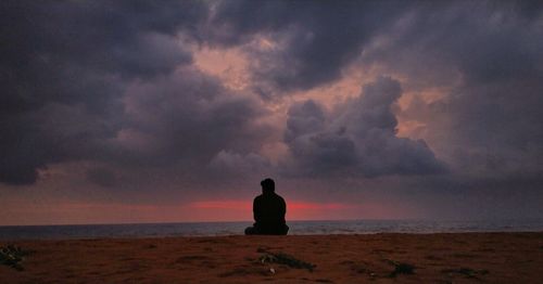Silhouette of man looking at sea against sunset sky