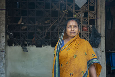 Portrait of a smiling young woman wearing sari standing against mud house in rural indian village