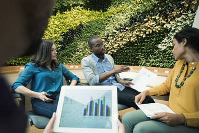 Young business people discussing in front of green plant wall