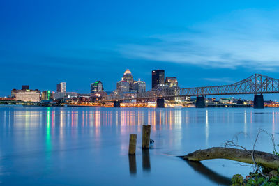 Illuminated modern buildings by bay against sky