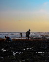 Men working at beach against sky during sunset