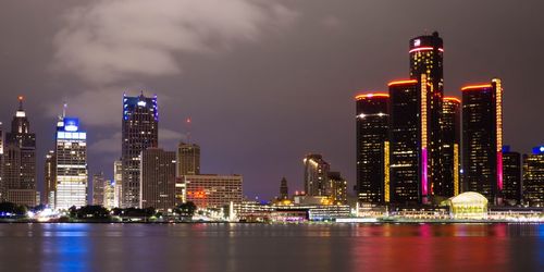 Illuminated buildings by river against sky in city at night