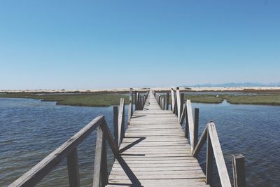 Pier over lake against clear blue sky