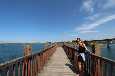 Portrait of woman standing on pier over lake against blue sky