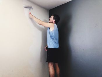 Side view of young man standing against wall at home