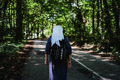 Rear view of woman walking on road amidst trees in forest