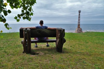 Rear view of man sitting on bench while looking at baltic sea