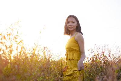 Portrait of smiling young woman standing on field against sky