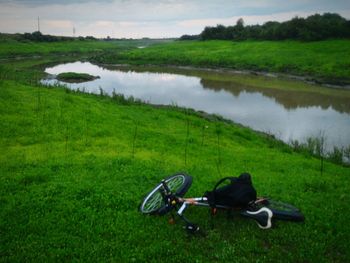 Bicycle on grassy field by lake against sky