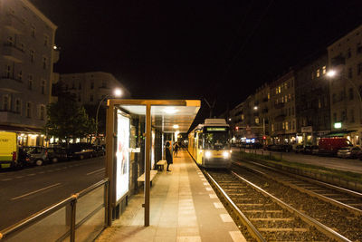 Illuminated railroad station by street against sky at night