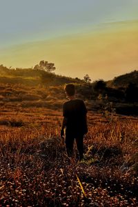 Rear view of man standing on field against sky during sunset