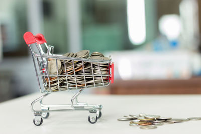 Close-up of miniature shopping cart with coins on table