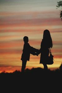 Silhouette of woman standing with her son at sunset