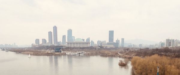 Buildings by river against sky in city