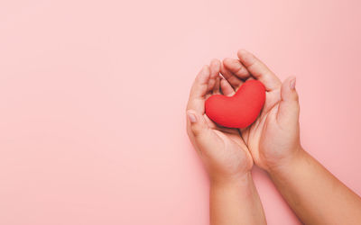 Close-up of woman hand holding heart shape against red background