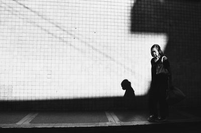 Full length of young woman using phone while standing against wall