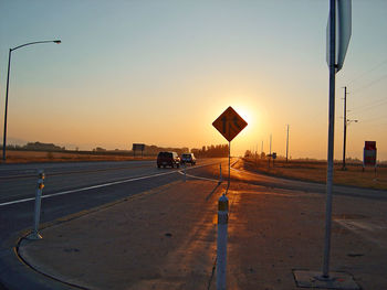 Road sign on street against clear sky during sunset