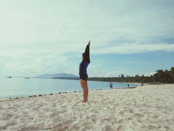 Full length of woman stretching on beach against sky