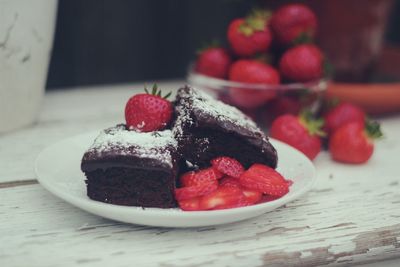 Close-up of brownie and sliced strawberries served on plate indoors