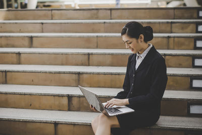 Businesswoman using laptop while sitting on steps in city