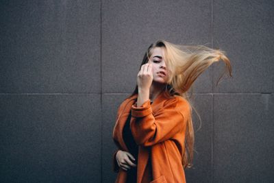 Woman with tousled hair standing against wall