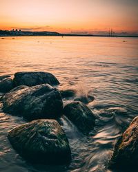 Rocks at sea shore against sky during sunset