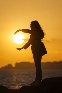 Silhouette woman standing by sea against sky during sunset