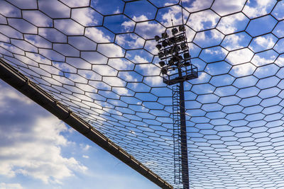 Low angle view of floodlight against sky seen through fence