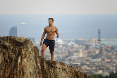 Physically challenged shirtless man looking away while standing on cliff against cityscape